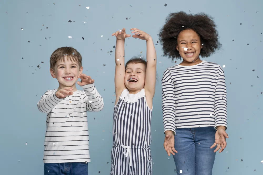 Three children laughing and throwing confetti against a blue backdrop