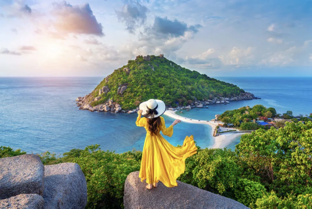 Traveller in a yellow dress at a viewpoint above a tropical island and turquoise bay