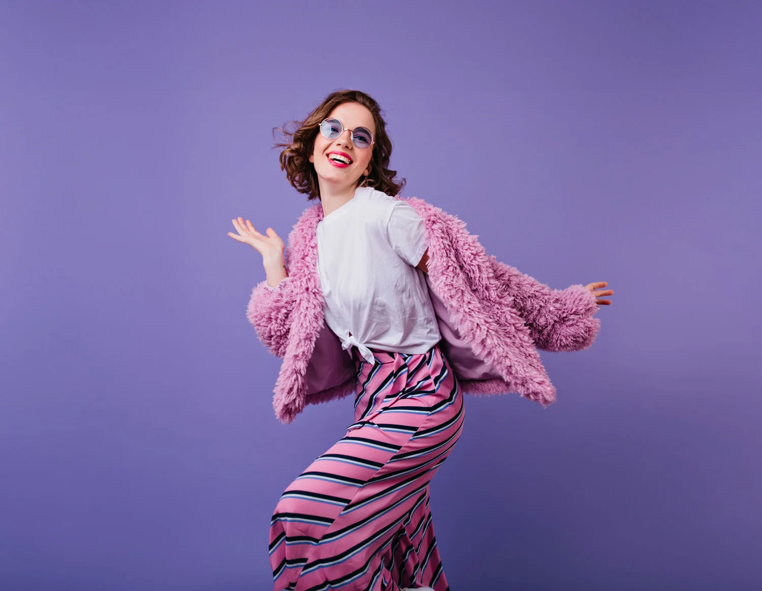 Model in a pink faux-fur jacket twirling against a purple studio backdrop