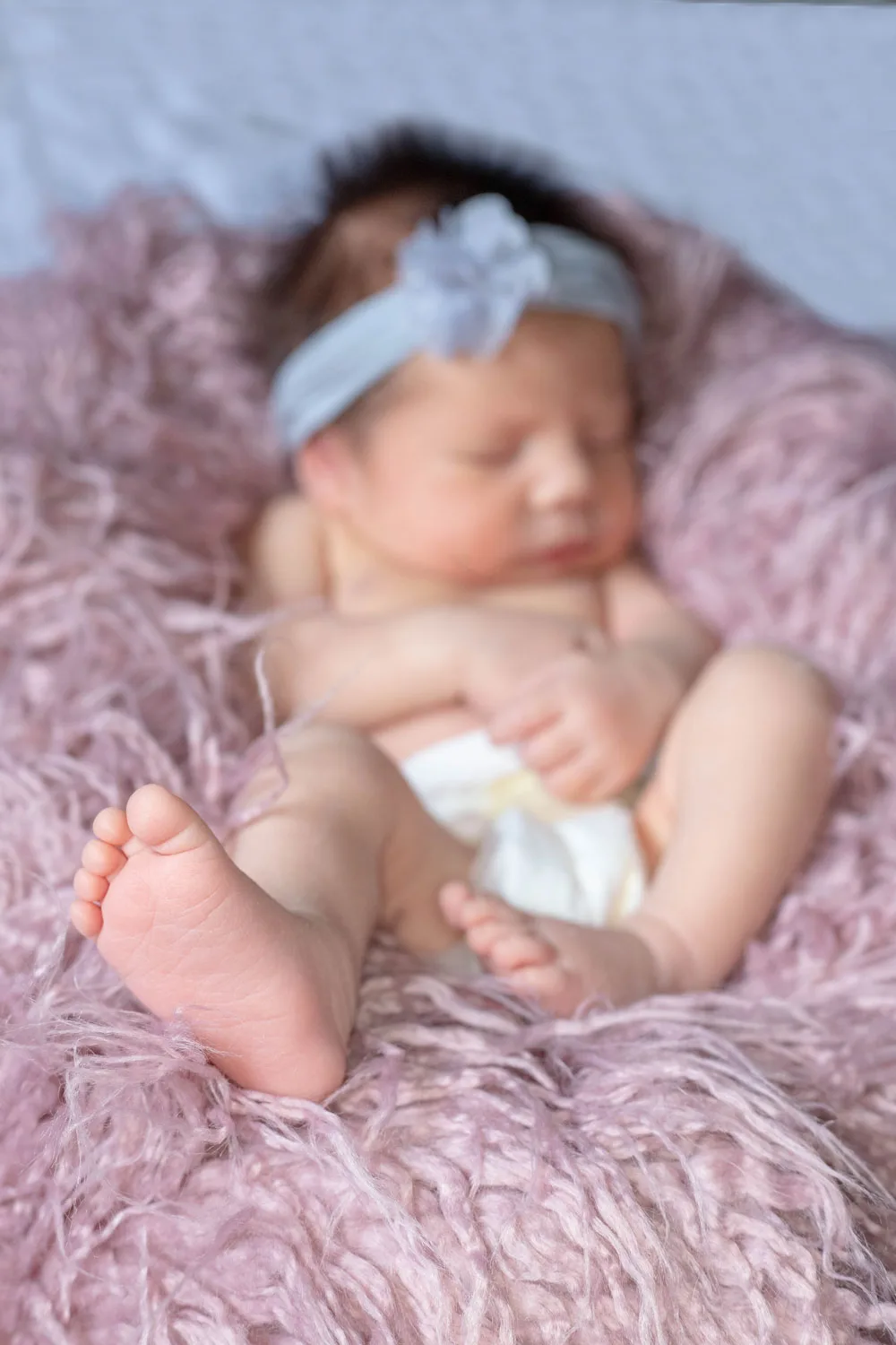 Newborn asleep in a bow headband on a soft pink blanket, baby photography Bangalore
