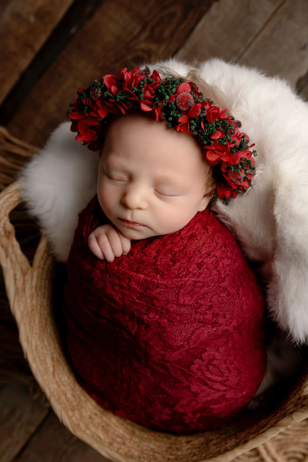 Newborn asleep in a red wrap with a floral crown in a wooden bowl, baby photoshoot Bangalore
