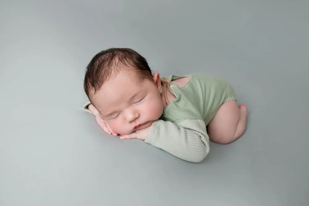 Newborn sleeping in a green outfit on a grey backdrop, newborn photography Bangalore