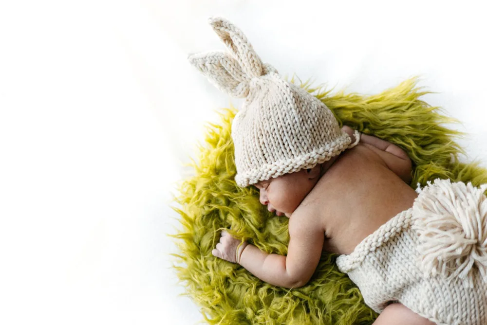 Newborn asleep in a knitted bunny bonnet on a green blanket, baby photoshoot Bangalore